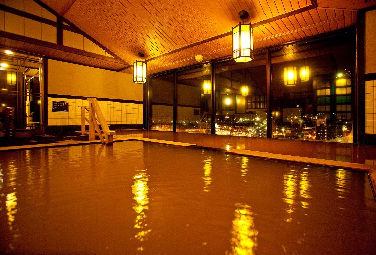 【大浴場/内湯】灯りに合う茶褐色の湯は美肌効果も。窓から見える夜景に心も癒されながら…