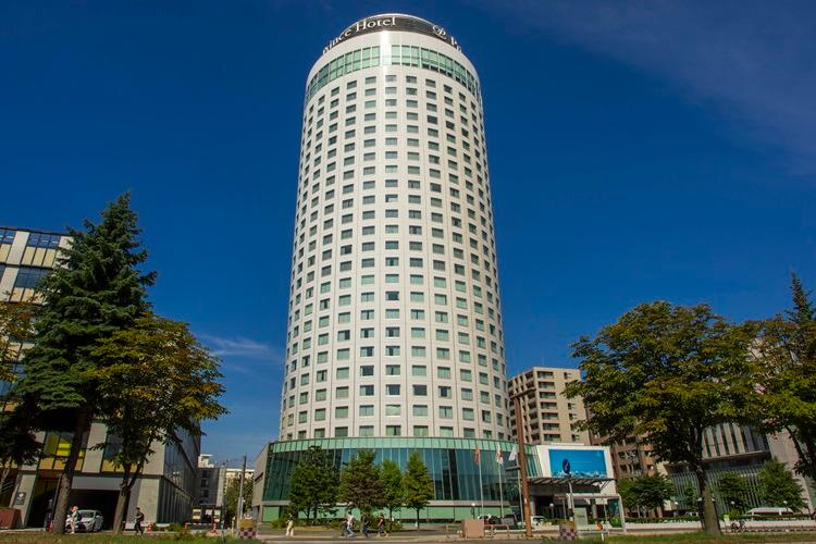 青空の下、札幌プリンスホテルが堂々と佇む日中の全景。円柱形のタワーは札幌の街並みに溶け込みます。