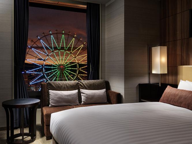 【観覧車側コーナーダブルルーム 22.2平米/ベッド幅160cm】シティビューを望むコーナーダブルはクイーンサイズのベッドと旅の疲れを癒すくつろぎのビューバス、独立した洗面・バスルームをご用意