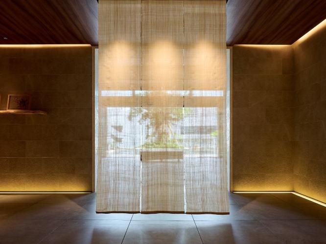 7Fでゲストを迎える芭蕉布のスクリーンと、その先に見える琉球アカギのベンチとシンボルツリーのガジュマル。